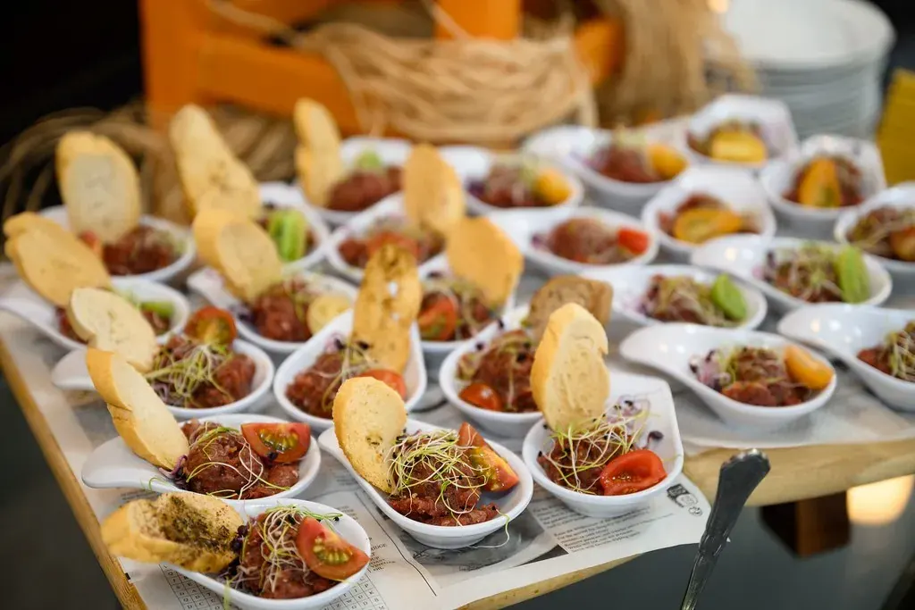 Az Ensana Grand Margitsziget catering szolgáltatása, ahol gourmet falatok láthatók fehér kanalakban tárhonnyal, paradicsommal és kenyérpálcikával