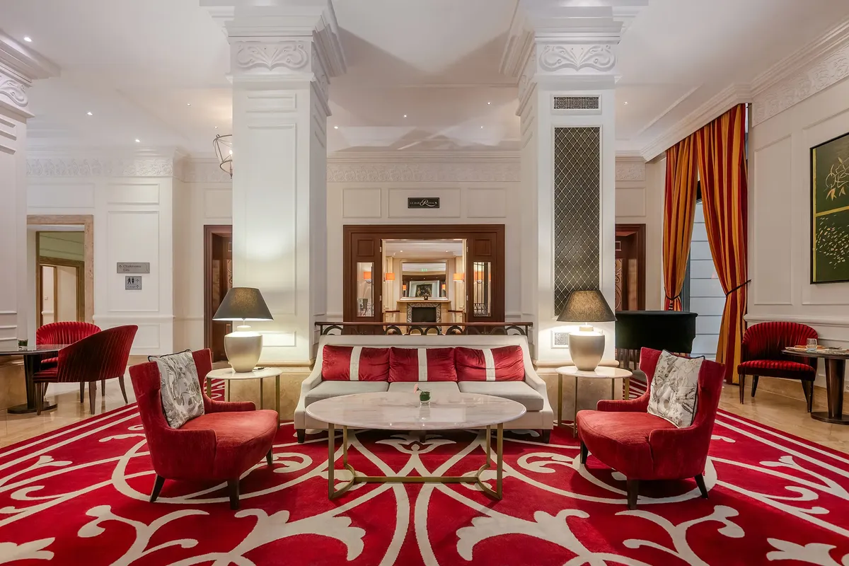 Corinthia Budapest lobby lounge, elegáns várakozó, piros fotelek, fehér oszlopok, luxus pihenőzóna