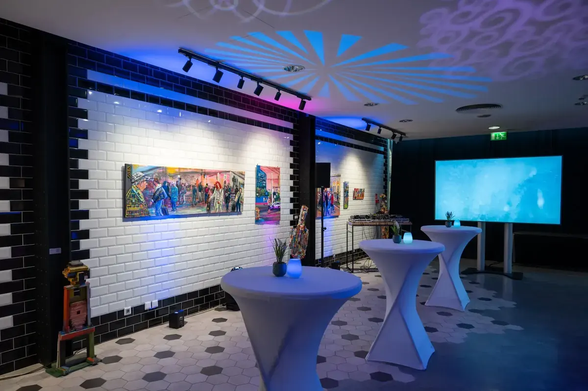 A Mercure Budapest Castle Hill lobby-ja művészeti kiállítással, ahol fehér és fekete csempefal, bárasztalok és kortárs magyar festmények láthatók kék LED világítással